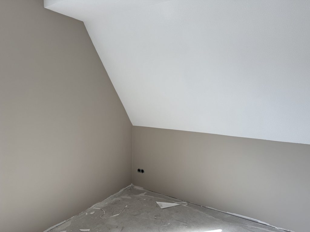 Zolderkamer met een schuine wand, de rechte muren al in een zachte beigetint afgewerkt