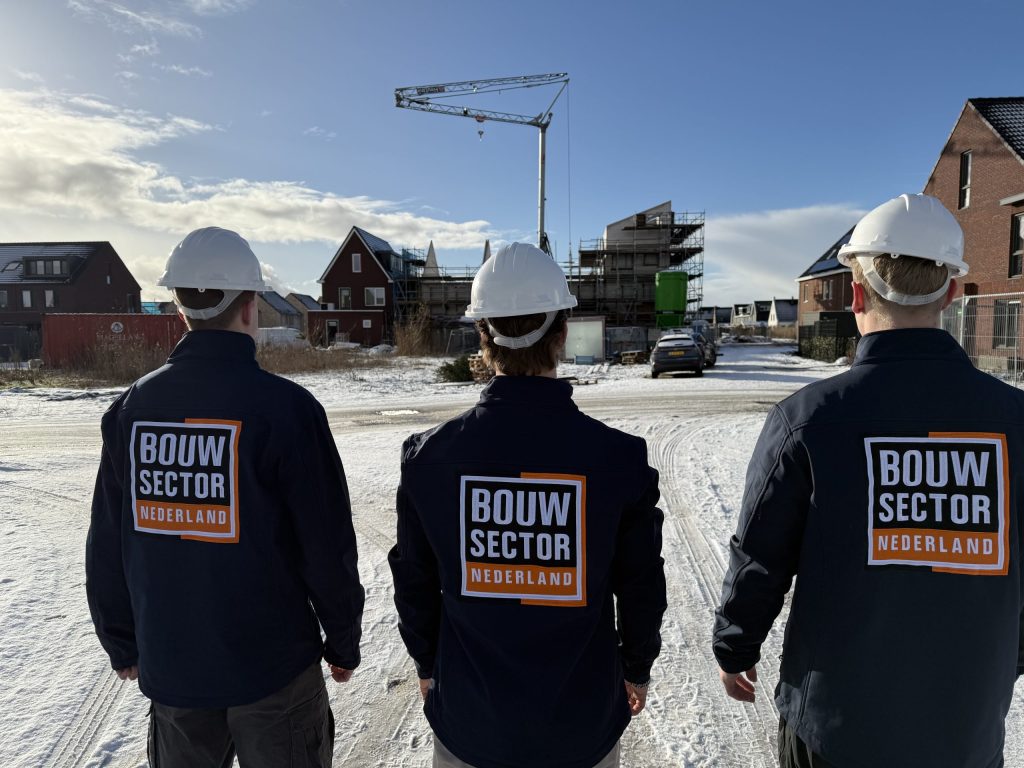 Drie vakmensen van Bouwsector Nederland met witte helm op een besneeuwde nieuwbouwstraat